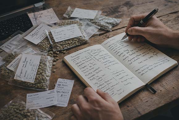 Notebook, papers, and sourcing notes on a table for coffee sourcing