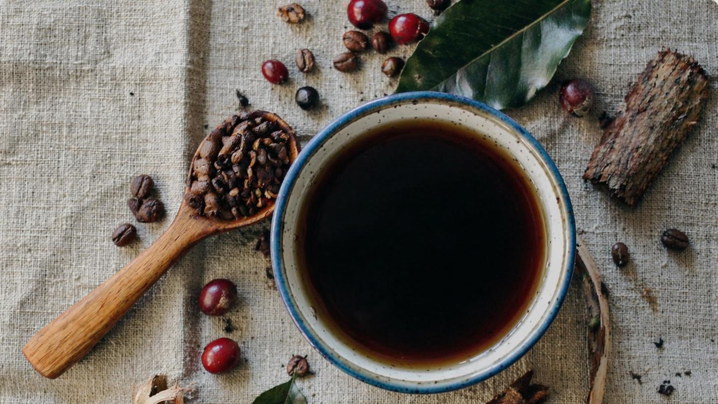 Cup of brewed coffee with roasted beans and coffee cherries on a linen surface, illustrating what to expect from coffee sourcing